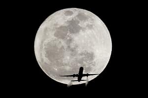 Airplane silhouetted against full moon