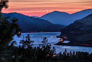 Crescent moon over river valley at sunset