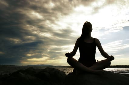 Silhouette of person meditating on rocks at sunset