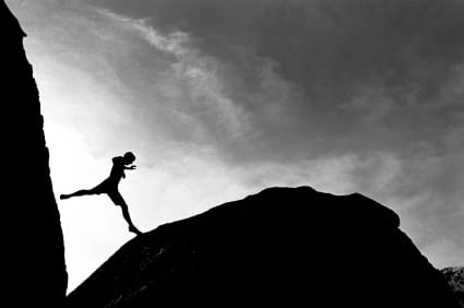 Silhouette of person leaping across rocky gap