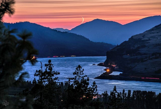 Crescent moon over river valley at sunset