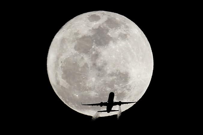 Airplane silhouetted against full moon