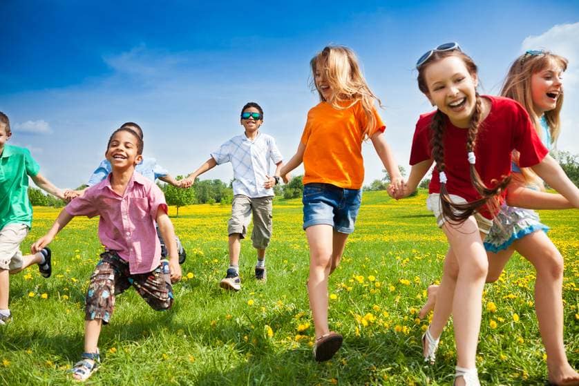 Children running hand-in-hand in sunny field